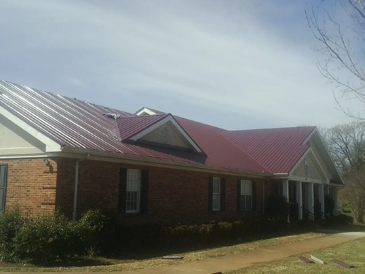 Red metal roof with gabled entries on a long brick building, from a Hail Damage Roof Repair job in Lagrangeville