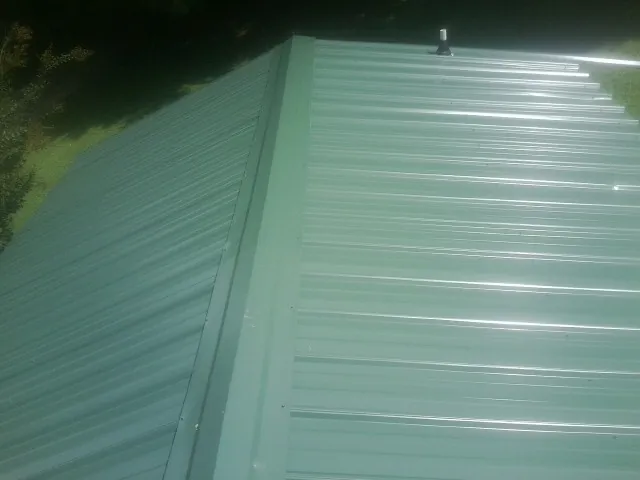 New green metal panels meeting at the ridge of a roof — Flat Roof Repair work by our crew in Lagrangeville