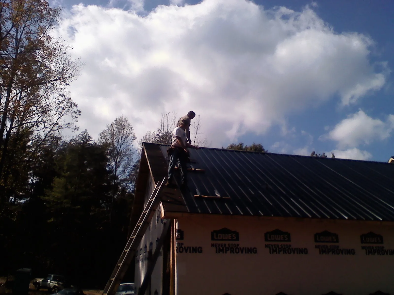 Roofer fastening dark metal panels high against a cloudy sky, from a Roof Inspection job in Lagrangeville