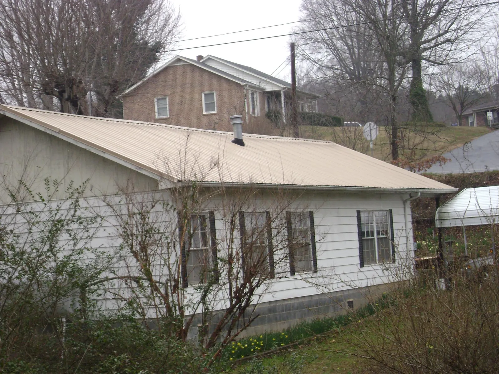 Tan metal roof on a white sided house set into a hillside — Commercial Roofing by Roofing Brothers in Lagrangeville